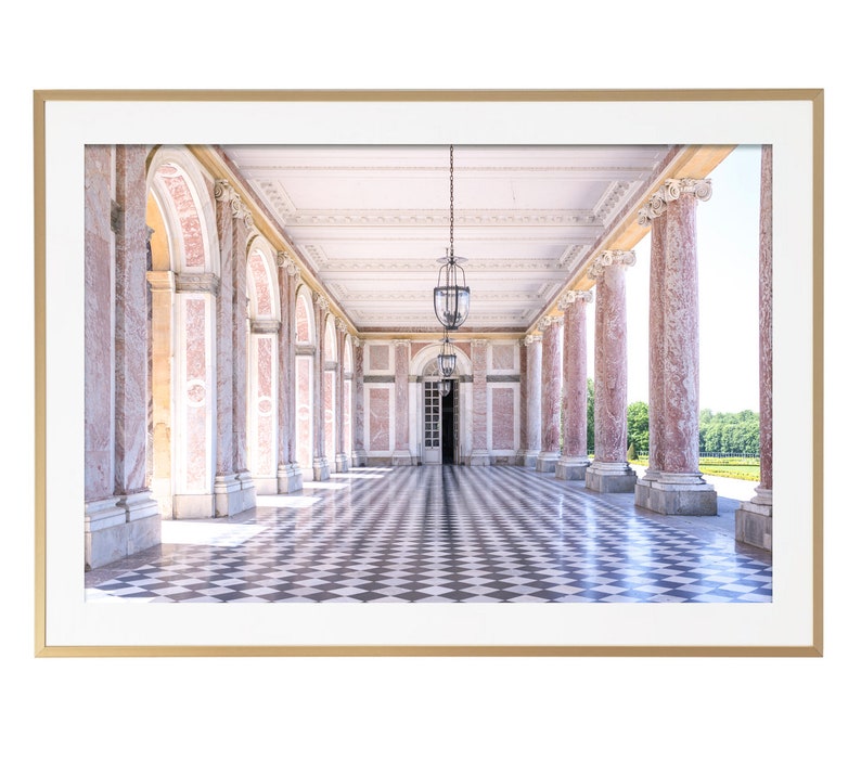 May include: A framed print of a classical colonnade with pink marble columns and a black and white checkered floor. Two ornate hanging lanterns illuminate the corridor. The print is set in a gold frame.