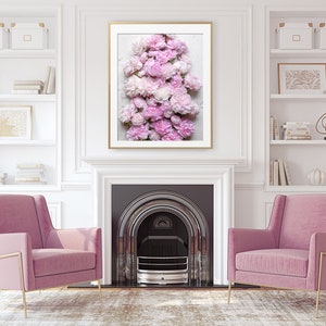 May include: A framed print of a cluster of pink peonies arranged in a vertical stack. The peonies are in various shades of pink, from light to dark. The print is hanging on a white wall above a fireplace.
