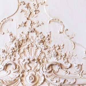 Puede incluir: Talla de madera ornamentada pintada de blanco con un dise&ntilde;o floral. La talla es de estilo rococ&oacute; y presenta detalles intrincados.