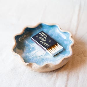 May include: A blue and white ceramic dish with a wavy edge, featuring a box of matches with the text "Love is in the air 40 Matches at Sinatra's".