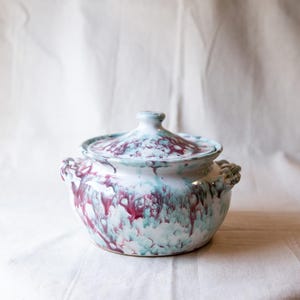 May include: A white ceramic casserole dish with a lid. The dish has a marbled design with pink and green swirls.