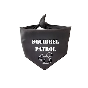 May include: A dark gray dog bandana with the words "SQUIRREL PATROL" in white block letters. Below the text is a white outline of a squirrel. The bandana is tied at the top.