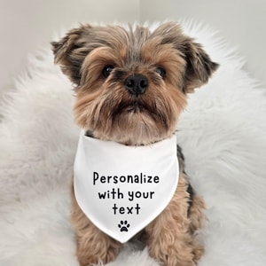 Personalize with your text dog bandana with a paw print at the bottom.  The dog is wearing a white bandana with black print.  These come in different colors and sizes.