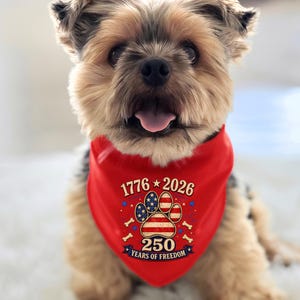 May include: A small dog wearing a bright red triangular pet bandana. The bandana features a central paw print graphic filled with a stars and stripes pattern, surrounded by the text 1776, 2026, and 250 YEARS OF FREEDOM with small bone icons.