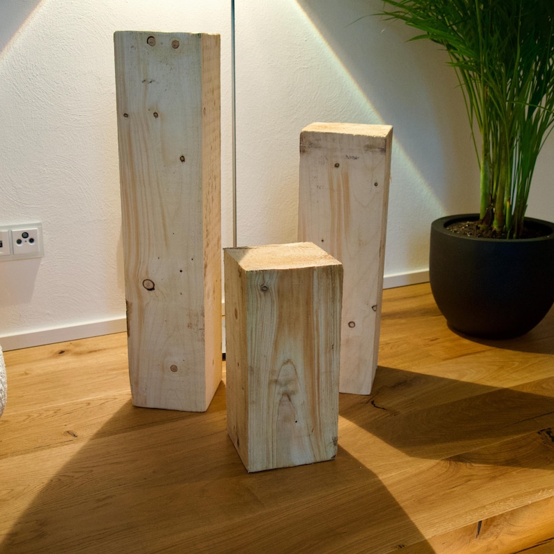 Peut inclure: Trois blocs de bois de tailles diff&eacute;rentes, empil&eacute;s sur un sol en bois. Les blocs sont en bois naturel de couleur brun clair.