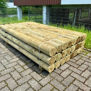 Puede incluir: Una pila de postes de madera para cercas, atados con cuerda, están dispuestos en una pila ordenada sobre una superficie de ladrillo gris. Los postes son todos del mismo tamaño y forma, y son de color marrón claro.