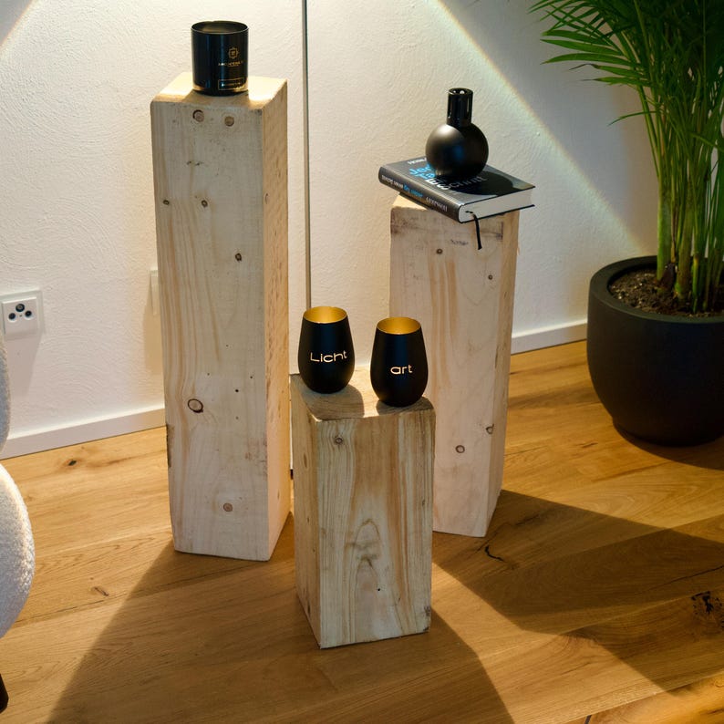 Peut inclure: Trois plateformes en bois de hauteurs diff&eacute;rentes, chacune avec un objet diff&eacute;rent sur le dessus. La plateforme la plus haute a une bougie noire, la plateforme du milieu a un livre et la plateforme la plus basse a deux tasses noires avec des lettres dor&eacute;es qui disent "Licht" et "art".