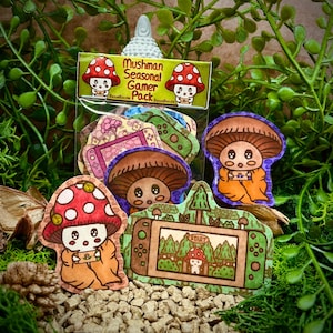 Peut inclure: Un paquet d'autocollants avec des motifs de champignons et de jeux vidéo. Les autocollants présentent un champignon avec un chapeau rouge et blanc à pois, une console de jeu et le texte "Mushman Seasonal Gamer Pack".