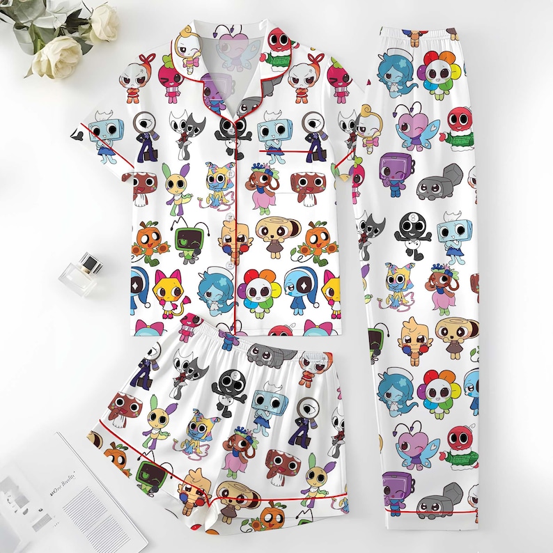 May include: White pajama set with a repeating cartoon character pattern in various colors. The set includes a short-sleeved button-up shirt, shorts, and long pants, all trimmed with red piping.