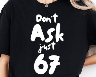 May include: Black t-shirt featuring the white text "Don't Ask just 67". The shirt has a relaxed fit, with a round neck and short sleeves. The text is in a bold, informal font.