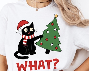 Puede incluir: Camiseta blanca con un gato negro de dibujos animados con un gorro de Papá Noel y una bufanda a rayas rojas y blancas, junto a un árbol de Navidad decorado. La palabra "WHAT?" está impresa en letras rojas debajo.