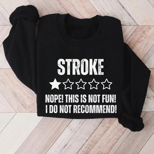 May include: Black sweatshirt with the word "STROKE" in large white letters. Below the word "STROKE" are five stars, with only one star filled in. The text "NOPE! THIS IS NOT FUN! I DO NOT RECOMMEND!" is below the stars.