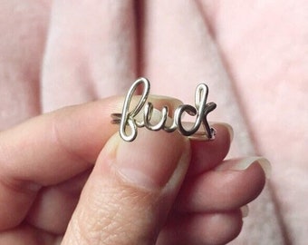 May include: A silver ring with the word "fuck" spelled out in cursive.