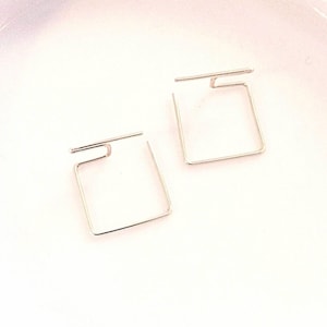 May include: A pair of silver square hoop earrings with a unique open design.