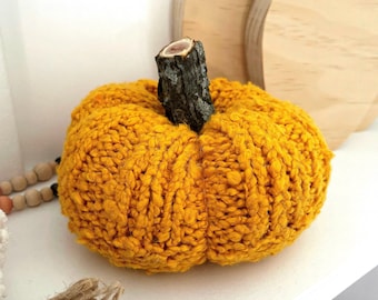 Pode incluir: Uma decoração de abóbora amarela texturizada feita à mão com um caule de madeira castanho escuro. A abóbora é feita de um fio grosso e em laçada. Um recorte de madeira em forma de abóbora está no fundo. Perfeito para decoração de outono.