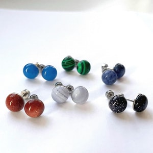 Könnte beinhalten: Sechs Paar Ohrstecker mit verschiedenen farbigen Steinen. Die Steine sind blau, grün, weiß, rot und schwarz.