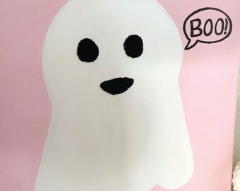 May include: A pink canvas painting with a white ghost with black eyes and a mouth saying "BOO!" in a speech bubble.
