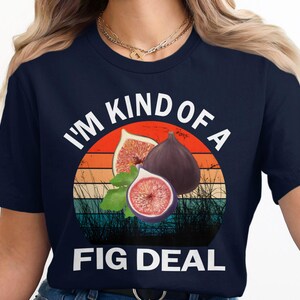 May include: A navy blue t-shirt with a white graphic of figs and a sunset. The text "I'm kind of a fig deal" is printed in white on the shirt.