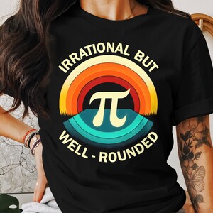 Peut inclure: T-shirt noir avec un graphique arc-en-ciel et le texte "Irrationnel mais bien arrondi" avec un symbole pi au centre.