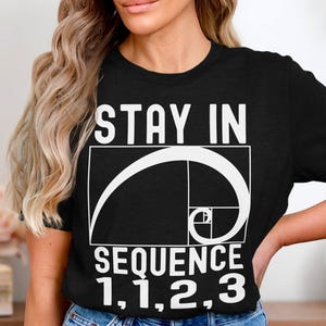 Könnte beinhalten: Schwarzes T-Shirt mit weißem Text "Stay in Sequence 1,1,2,3" und einer weißen Grafik der Fibonacci-Spirale.