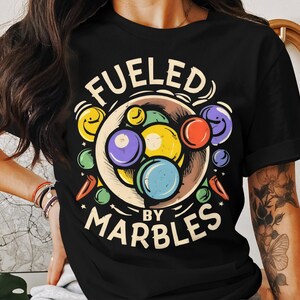 May include: Black t-shirt with a graphic of a bowl of colorful marbles and the text "Fueled by Marbles".