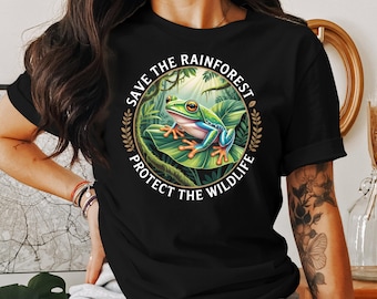 May include: Black t-shirt featuring a vibrant illustration of a tree frog on a large leaf, surrounded by lush greenery. The design includes the text "SAVE THE RAINFOREST PROTECT THE WILDLIFE" in a circular arrangement, promoting environmental awareness.