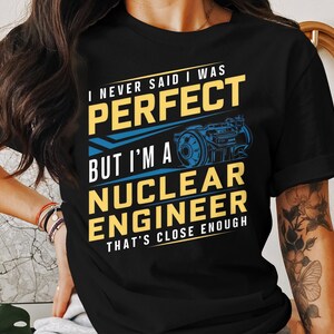Puede incluir: Camiseta negra con un diseño gráfico blanco y amarillo. El texto en la camiseta dice "Nunca dije que era perfecto, pero soy un ingeniero nuclear, eso está bastante cerca".