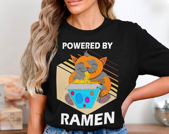 May include: Black t-shirt featuring a white graphic of a cat eating ramen noodles. The text "Powered by Ramen" is printed in white below the image.