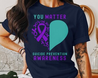 May include: A navy blue t-shirt with the text "You Matter" and a teal heart with purple ribbon designs. The text "Suicide Prevention Awareness" is also printed on the shirt.