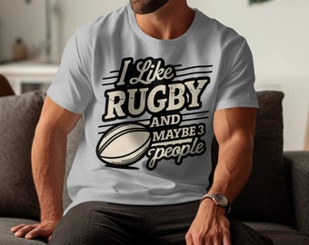 May include: A grey t-shirt with a black graphic that says "I like rugby and maybe 3 people". The graphic also includes a black and white illustration of a rugby ball.