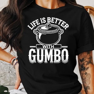 May include: Black t-shirt with white text that reads "Life is better with Gumbo". A white illustration of a pot of gumbo is above the text.