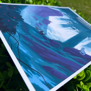 K&ouml;nnte beinhalten: Ein Druck mit einer Fantasielandschaft in Blau- und Lilat&ouml;nen. Das Kunstwerk zeigt einen H&uuml;gel mit stilisierten B&auml;umen, einem gro&szlig;en Mond und mehreren kleinen katzenartigen Kreaturen. Der Druck ist auf wei&szlig;em Papier.