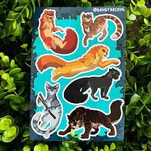 Op de afbeelding: Een stickervel met zes gestileerde kattenillustraties in verschillende poses en kleuren. De katten variëren van oranje en bruin tot zwart en grijs, met gedetailleerde vachtpatronen. De achtergrond is een turquoise raster met een donkerblauwe rand en de tekst "@genstaelens".