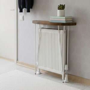 Puede incluir: Una entrada moderna con una puerta blanca, un perchero de pared con una chaqueta azul marino y un bolso tote marrón. Una pequeña mesa redonda con tapa de madera y radiador debajo.