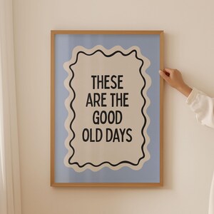 May include: A framed print with a light blue background and a white border. The print features black text that reads "These are the good old days" in a wavy, decorative frame.