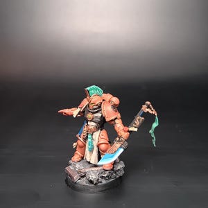 May include: A detailed miniature warrior figure in red and silver armour, wielding a blue-bladed sword. The figure has a green crest and stands on a textured base. The design suggests a fantasy or sci-fi setting.