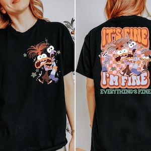Może przedstawiać: Czarny t-shirt z kreskówkową grafiką przedstawiającą trzy zmartwione postacie i napisem "It's Fine, I'm Fine, Everything's Fine" na plecach. Przód koszulki ma mniejszą wersję grafiki. Projekt wykorzystuje odcienie pomarańczu, różu i fioletu.