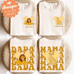 May include: Four cream-colored t-shirts with Lion King-themed designs. Two shirts feature a lion and the word "Dada," and the other two feature a lioness and the word "Mama." The designs are in shades of yellow and brown.