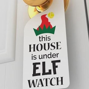 May include: A white door hanger with the text "this HOUSE is under ELF WATCH" in black. The top of the hanger features a green and red graphic of a Christmas elf hat. The hanger is attached to a gold door knob.