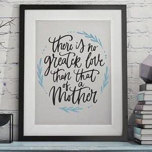 May include: A black framed wall art print featuring the black cursive text There is no greater love than that of a Mother on a light gray background, accented with light blue leaf illustrations arranged in a circular pattern around the lettering.