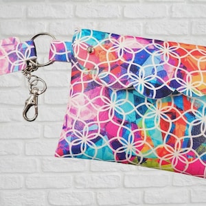 May include: A small rectangular pouch featuring a vibrant multicoloured geometric pattern with a white interlocking floral design. The pouch has a scalloped flap with two silver metal studs and is attached to a matching strap via a silver metal ring.