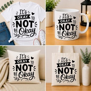 Può includere: Una collezione di articoli con la frase "It's okay to not be okay" in nero. Include una maglietta bianca, una tazza da caffè bianca, un cuscino color crema e una borsa tote in tela. Gli articoli sono disposti su una superficie di legno.