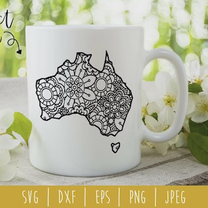 May include: White ceramic mug with a black, detailed outline of Australia filled with a floral mandala design. The mug has a curved handle and the words "project idea" are written in a script font. White flowers and green leaves are in the background.