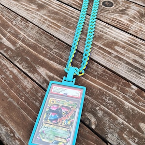 May include: A turquoise necklace with a matching card holder. The holder encases a Pokemon card with the text "M Venusaur EX". The chain is made of turquoise, yellow, and blue links. The card holder has the text "2016 Pokemon XY Evolutions".