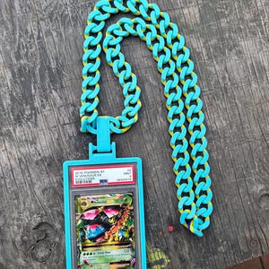 May include: A turquoise chain necklace with yellow accents, holding a graded Pok&eacute;mon card. The card is in a blue plastic case and features a colorful illustration of a Venusaur EX card from the 2016 Pok&eacute;mon XY Evolutions set.