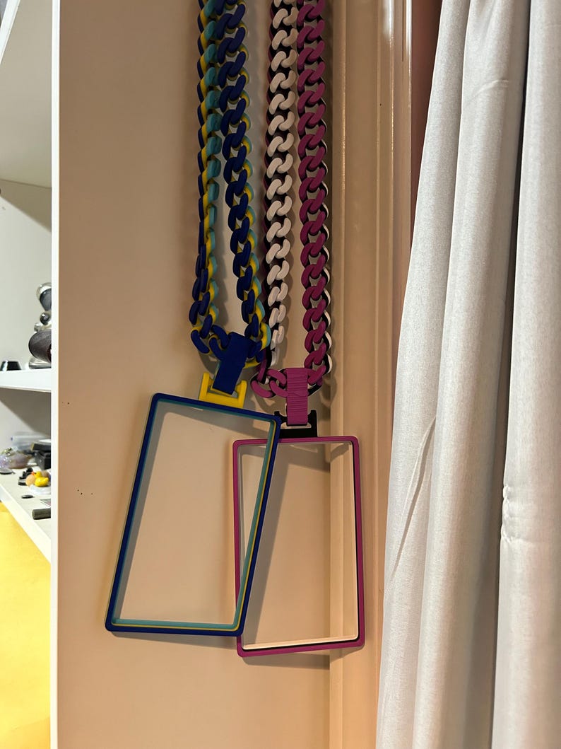 May include: Three colorful necklaces with matching rectangular frames hanging on a wall. The necklaces are blue, white, and pink, with coordinating frames in blue, pink, and white. The frames are empty.