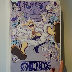 Peut inclure: Un classeur rectangulaire blanc orné d'une illustration animée vibrante avec plusieurs personnages dans des tons de violet, blanc et bleu. Le personnage central rit, vêtu de blanc, entouré de diverses créatures et du logo One Piece.