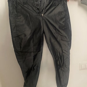 May include: Black trousers with a button fly and a zip. The trousers have a shiny, almost satin-like finish.