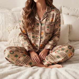 May include: A long-sleeve button-down pajama shirt and matching pants set featuring a tan and brown checkered pattern with festive holiday icons including Santa Claus faces, green wreaths, wrapped gift boxes, and yellow bells throughout.