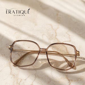 May include: Square-framed eyeglasses with a light brown translucent frame and gold-colored arms. The brand name "ERATIQUE EYEWEAR" is printed in black at the top. The glasses are set against a light-colored, textured background.